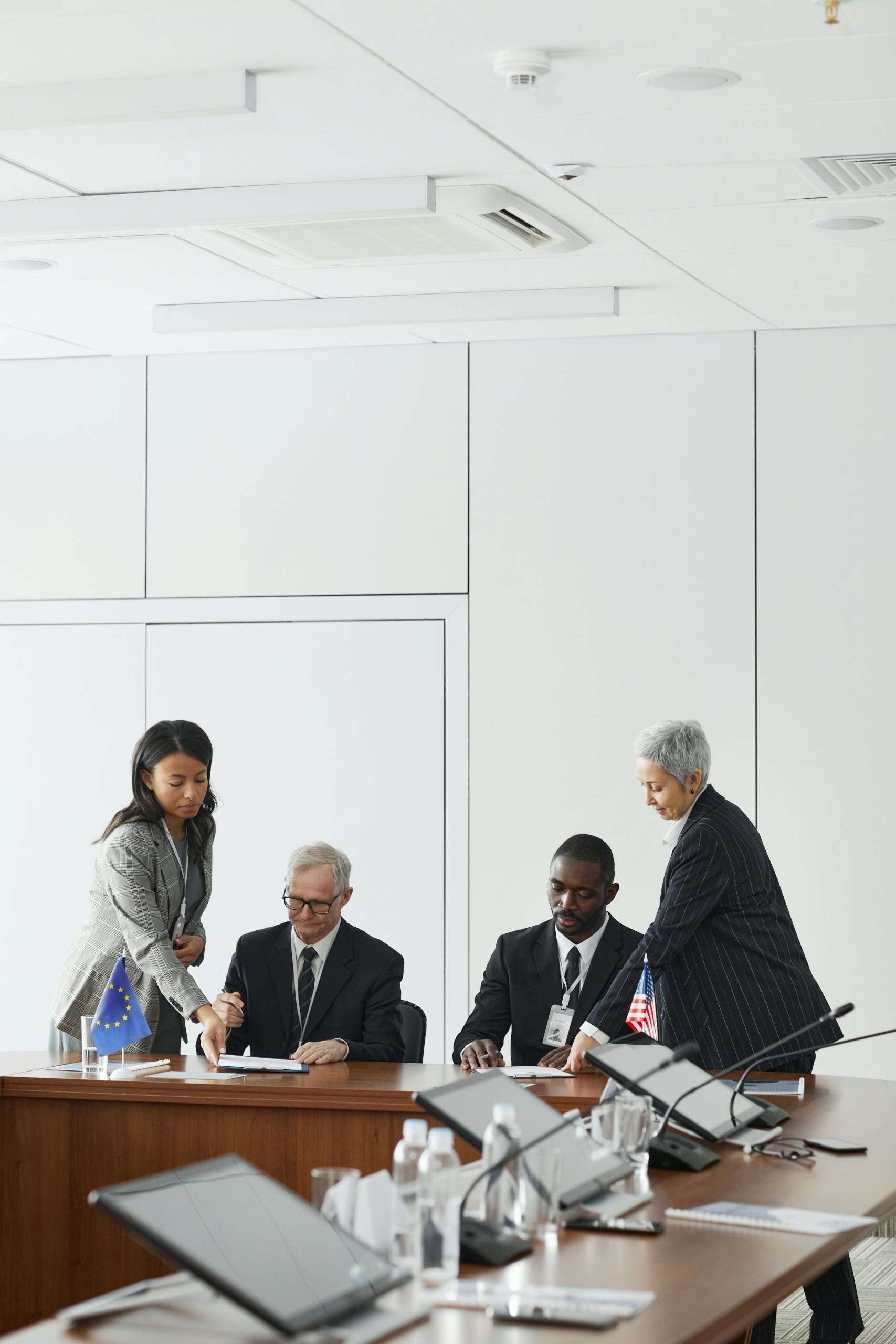 Four people in professional attire participate in a formal signing ceremony at a conference table featuring U.S. and EU flags.
