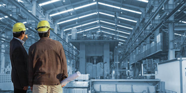 two men speaking about cost segregation in warehouse with construction hats, one pointing in the distance