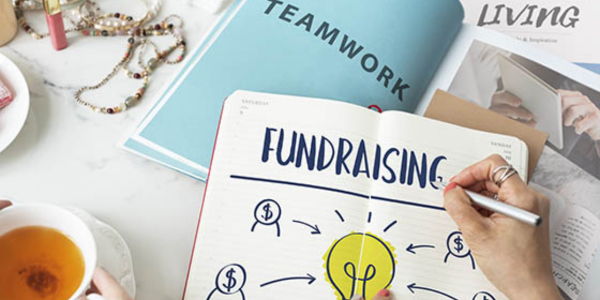 person writing "fundraising" in notebook