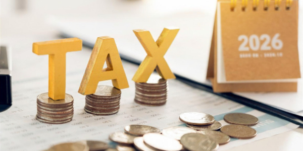 yellow building letter blocks reading 'TAX' balancing on stacks of quarters with 2026