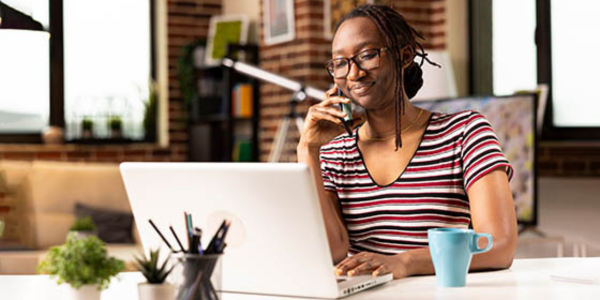 self-employed woman sitting at a table with a laptop and mug, while holding a cellphone