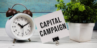 Sign that reads 'Capital Campaign' with alarm clock and plant next to it