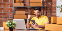 person at table with laptop open with phone in hand, celebrating from doing well from sideline activity